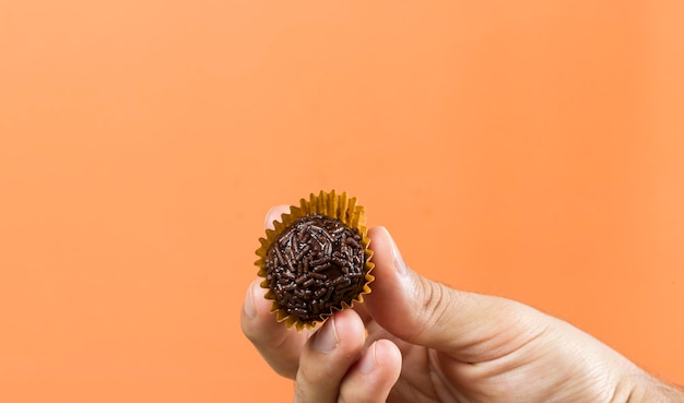 De hand van een vrouw met een veganistische brigadeiro Typische Braziliaanse zoete oranje achtergrond