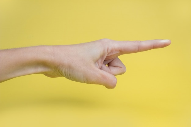 De hand van een vrouw met een wijsvinger op een gele achtergrond.