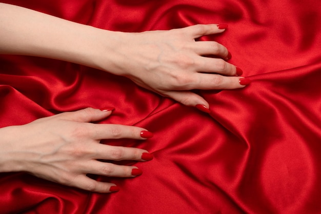 De hand van een vrouw met rode nagels probeert een rode zijden stof eraf te trekken