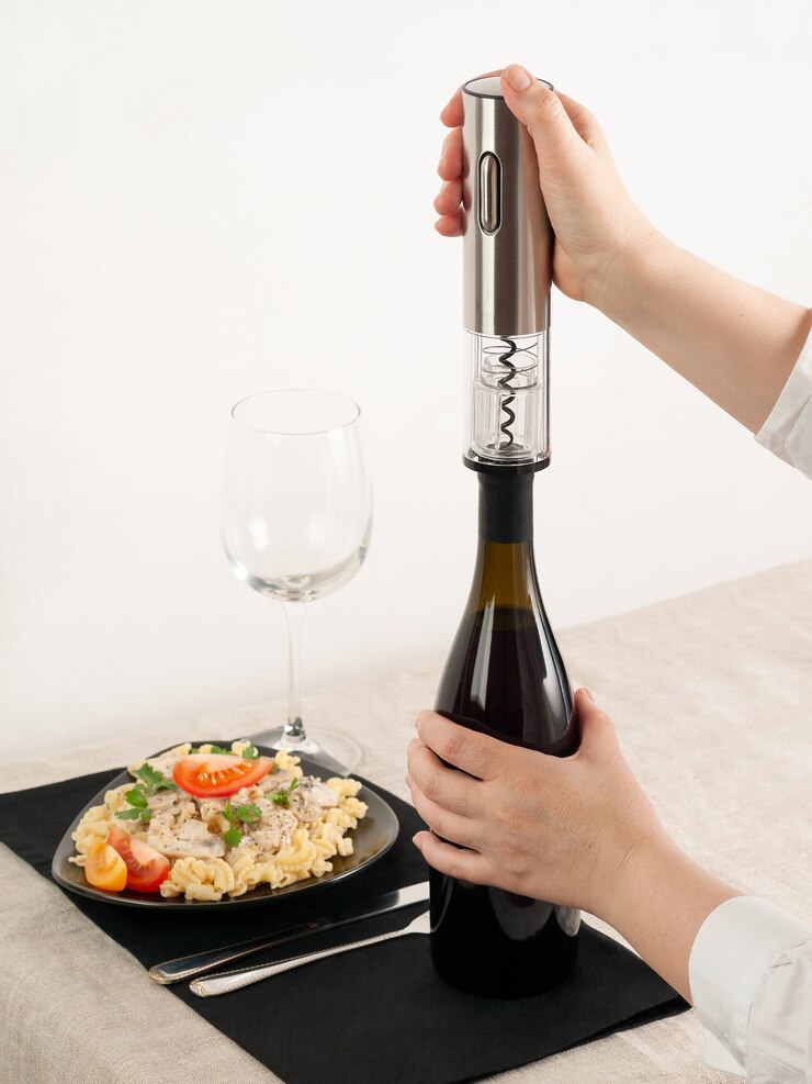 De hand van een vrouw opent een fles wijn met een elektrische kurkentrekker van grijs metaal