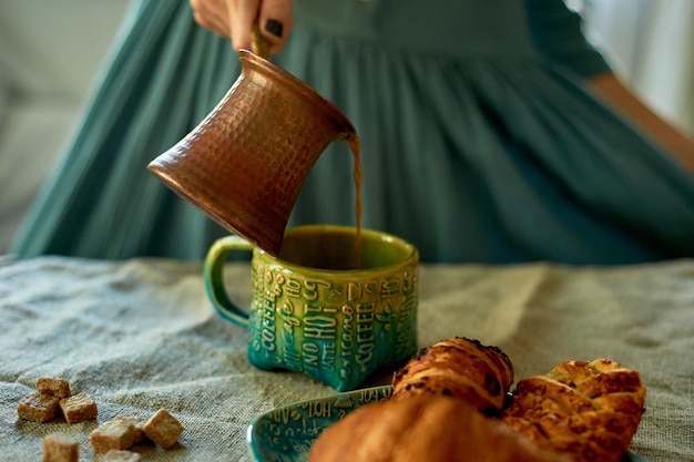 De hand van een vrouw schenkt koffie gebrouwen in turkrustieke eenvoud