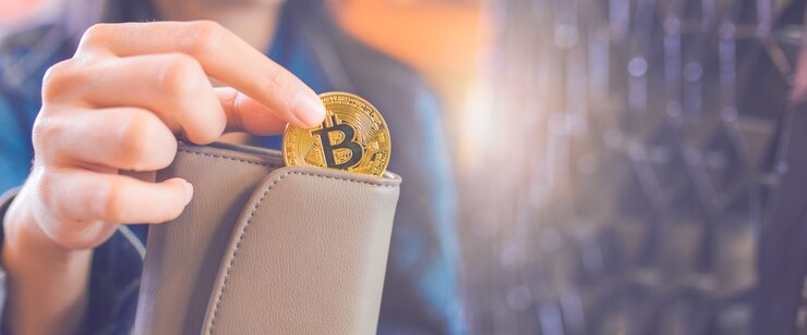 De hand van een vrouw trekt een bitcoin-munt uit een portefeuille.
