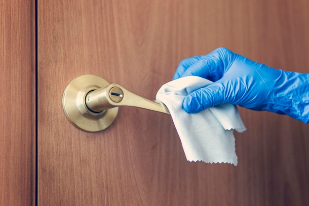 De hand van een vrouw veegt de deurklink af met een natte doek. De meid wast de deurknop. Preventie van coronavirus en bacteriële infecties