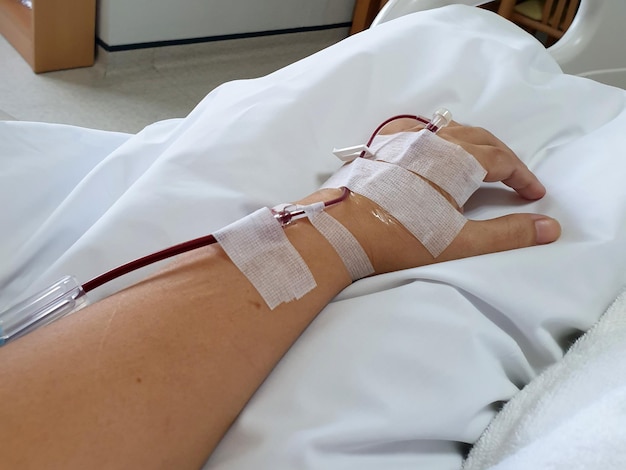 De hand van een vrouwelijke patiënt met een stokbuis van de transfusie van bloed in een ziekenhuiskamer