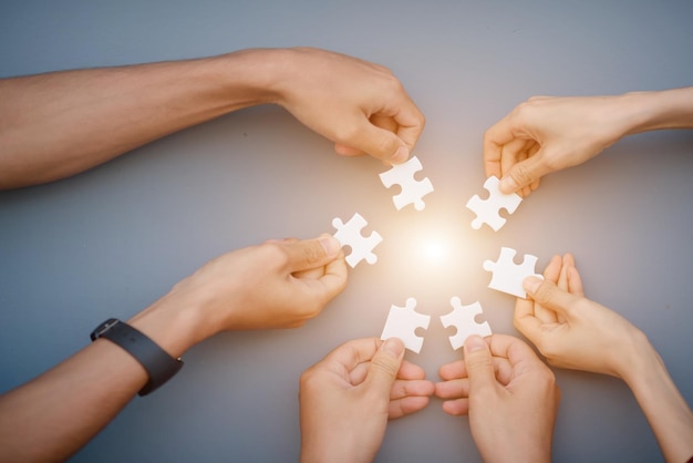 De hand van een zakenman die een papieren puzzel vasthoudt en de puzzel samen oplost het zakelijke team heeft een legpuzzel samengesteld een bedrijfsgroep die de puzzelstukjes wil samenbrengen