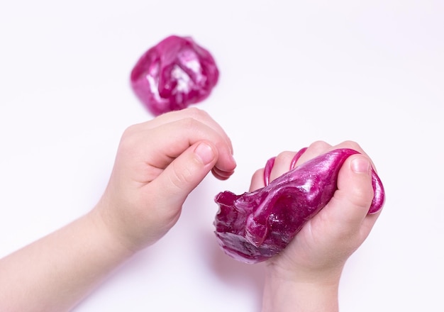 De hand van het kind knijpt in een kleurrijk paars slijmspeeltje Uitzicht van boven Plat leggen