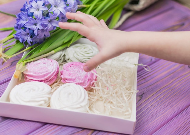 De hand van het kind reikt naar een snoepdoos met een marshmallow zephyr