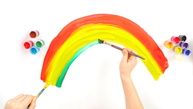 De hand van het kind tekent een regenboog op een witte achtergrond. creatief werk