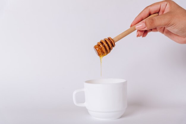 De hand van het meisje houdt een Honey Dipper op een witte beker