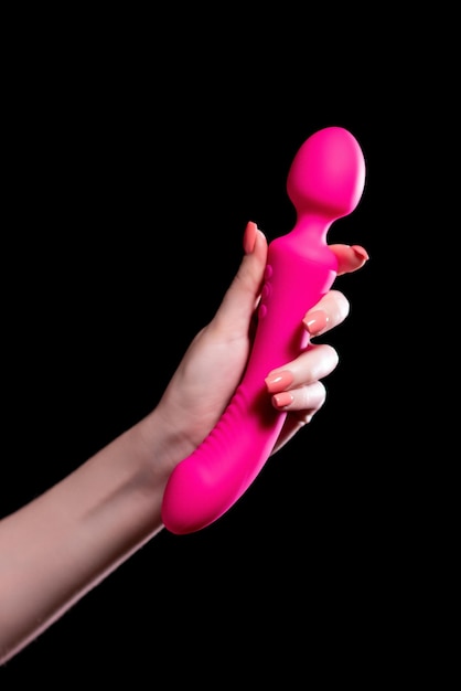 De hand van het meisje houdt een roze stimulator vast voor seks op een zwarte geïsoleerde achtergrond Vibrator voor masturbatie Dildo voor stimulatie Afbeelding voor seksshop