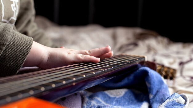 De hand van kinderen op de hals van een oranje kleur van akoestische gitaar. het instrument leren spelen.