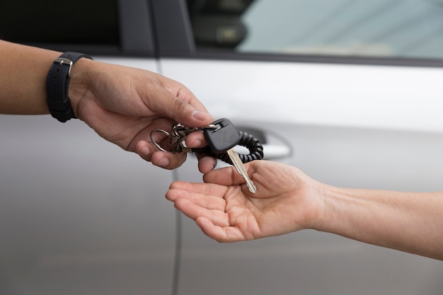 De hand van mensen geeft en krijgt autosleutel met autoachtergrond