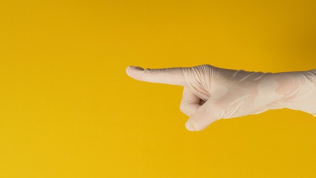 De hand wijst met de vinger en draagt een medische handschoen op een gele achtergrond. Studio-opnamen.