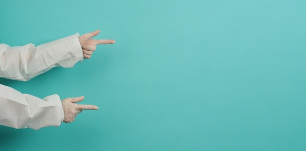 De hand wijst met de vinger en draagt medische handschoenen en een PPE-pak op een blauwe en groene of Tiffany Blue-achtergrond.