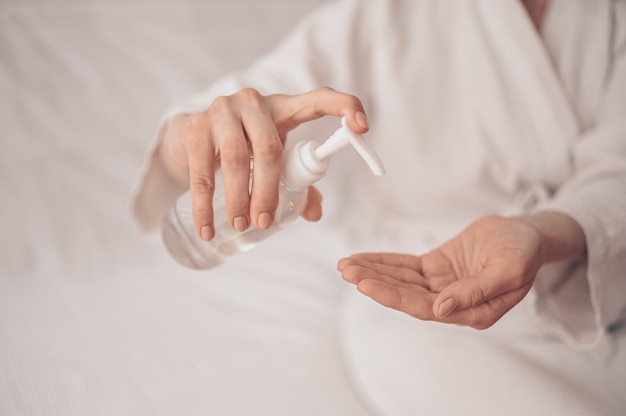 De handdesinfecterende vrouw die de desinfecterende vloeistof van het alcoholgel toepassen die vrouwelijke handen wrijven maakt thuis persoonlijke hygiënecoravirus pervention schoon. Fles met ontsmettingsmiddel. Stop het COVID19-concept