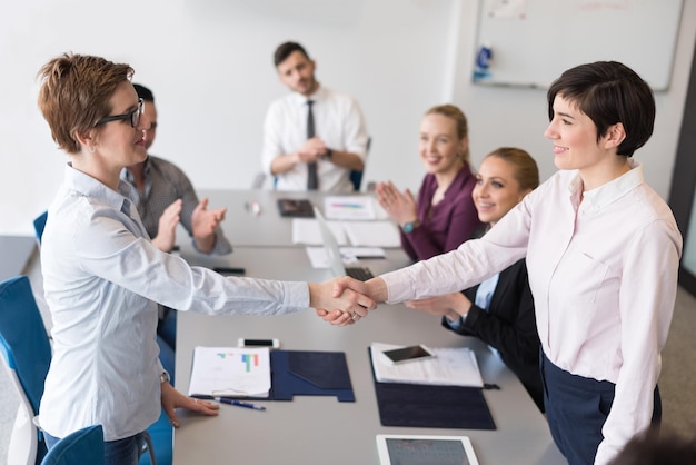 De handdruk van zakenvrouwen op teamvergadering met een groep mensen vervaagd op de achtergrond bij het interieur van een modern opstartend kantoor