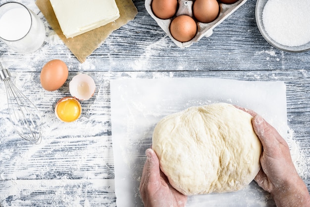 De handen die met het receptbrood, broodjes, pizza of pastei werken die van de deegvoorbereiding ingridients, voedselvlakte maken leggen op achtergrond van de keuken de grijze houten lijst.