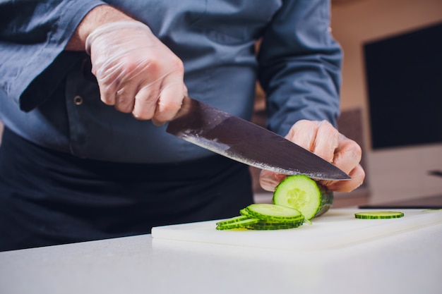 De handen die van cook verse komkommer op houten raad snijden