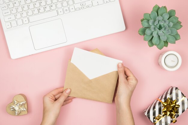 De handen die van de vrouw ambachtenvelop met copyspace op roze de bovenkantmening houden van de pastelkleurlijst. Plat lag compositie voor Valentijnsdag.