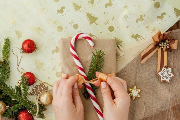 De handen die van de vrouw Kerstmisgift verpakken, sluiten omhoog. Onbereide kerstcadeautjes op houten met decorelementen en items, bovenaanzicht. Kerstmis of Nieuwjaar DIY-verpakking.