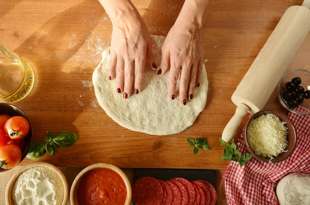 De handen die van de vrouw pizza thuis koken, toevoegend alle ingrediënten