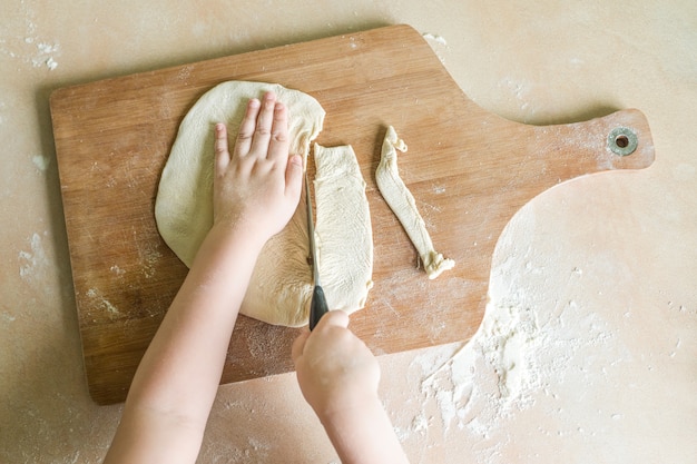 De handen die van kinderen ruw gerold deeg snijden