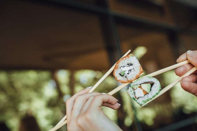 De handen die van vrouwen houten stokken met sushi houden