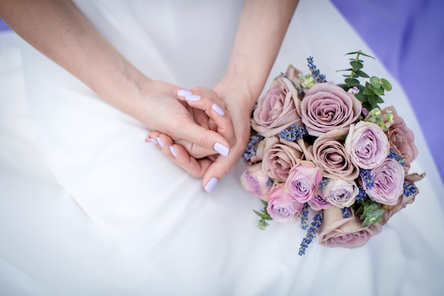 De handen van de bruid naast het boeket op de achtergrond van de trouwjurk