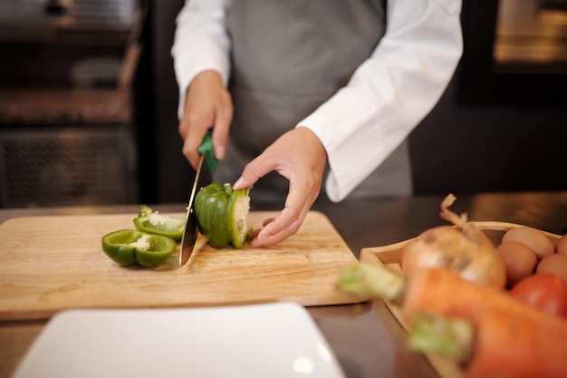 De handen van de chef-kok hakken groene peper in grote stukken