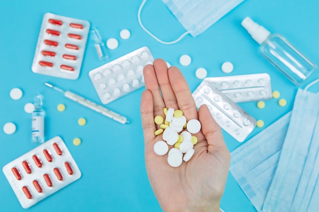 De handen van de dokter houden pillen vast. remedie voor coronavirus. Medische remedies in de strijd tegen covid-19. Pillen, spuiten, thermometer, medische masker op blauwe tafel.