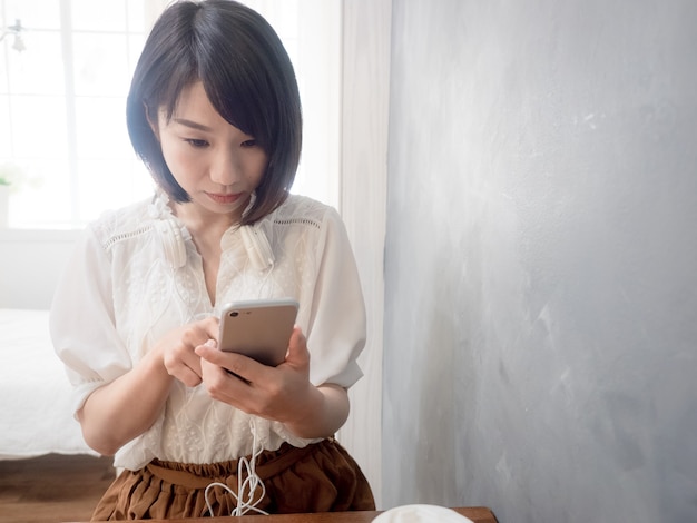 De handen van de jonge aziatische vrouw met mobiele telefoon