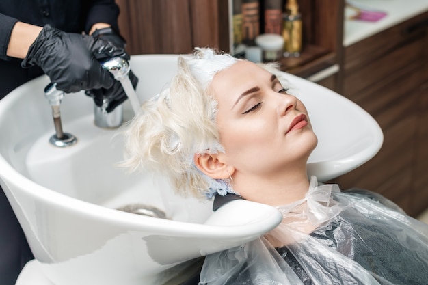 De handen van de kapper wassen het haar van een vrouw in een gootsteen na haarkleuring.