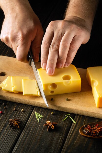 De handen van de kok met een mes snijden melkkaas op een snijplank Keuken Zuivelproducten koken met peper en rozemarijn voor een heerlijke lunch in de keuken van een restaurant