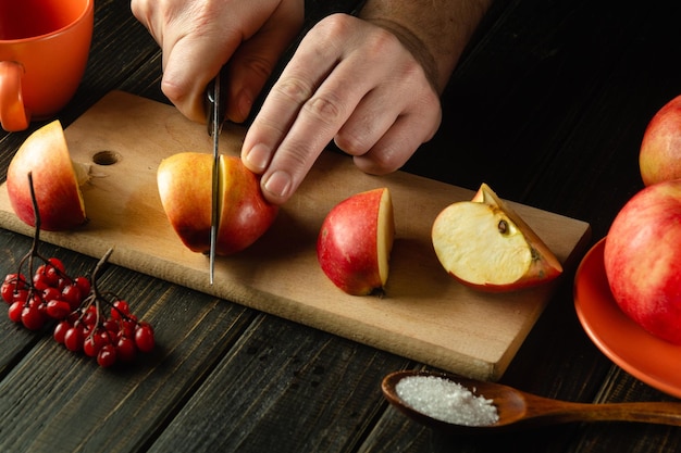 De handen van de kok op de keukentafel met een mes snijden verse appels op een snijplank