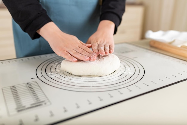 De handen van de kok staan klaar om het tarwedeeg te kneden op een siliconen bakmat met verschillende markeringen voor gebruiksgemak