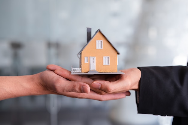 De handen van de makelaar in onroerend goed bieden huis aan koper aan.