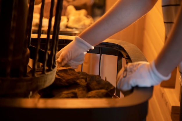 De handen van de meester legden stenen in de saunakachel. detailopname