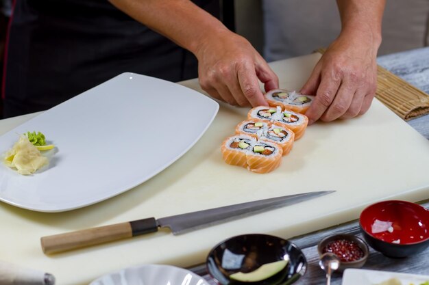 De handen van de mens raken sushibroodjes aan. Witte plaat op kookbord. Uramaki-broodjes bereid door kok. Favoriet gerecht van fijnproevers.