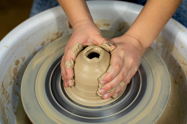 De handen van de pottenbakker van de vrouw gevormd door een aarden pot op een pottenbakkersschijf. De pottenbakker werkt in een werkplaats.