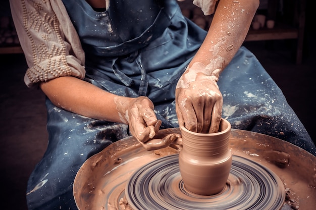 De handen van de pottenbakker zijn gevormd tot een beker van klei. het proces van het maken van aardewerk op een pottenbakkersschijf.