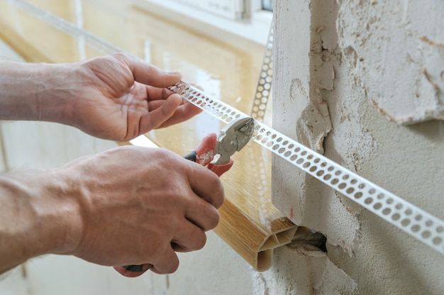 De handen van de werknemer snijden een geperforeerde aluminium hoek