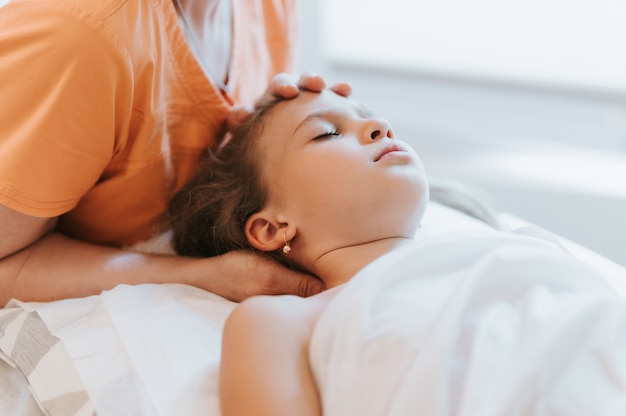 De handen van echte artsenosteopaten doen fysiologische en emotionele therapie voor een achtjarig meisje. pediatrische osteopathie behandelsessie. alternatief medicijn. zorgen voor de gezondheid van het kind