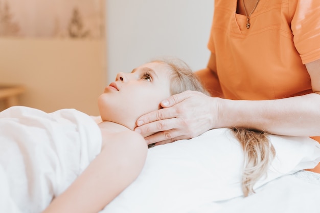 De handen van echte artsenosteopaten doen fysiologische en emotionele therapie voor een achtjarig meisje. pediatrische osteopathie behandelsessie. alternatief medicijn. zorgen voor de gezondheid van het kind