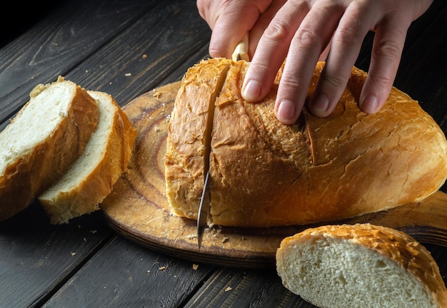 De handen van een chef-kok snijden met een mes vers tarwebrood voor het ontbijt of de lunch