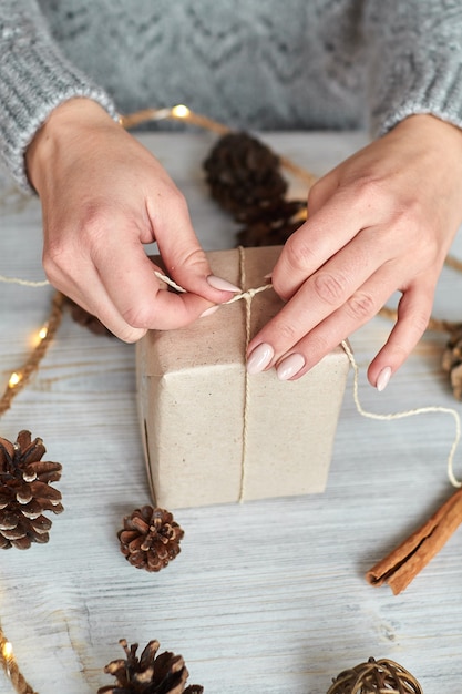 De handen van een jonge vrouw maken en verpakken kerst- en nieuwjaarscadeaus voor de vakantie. Cadeautjes aan familieleden en vrienden met felicitaties