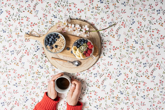 De handen van een jongen met een kopje koffie en yoghurt met fruit op een bed. kopieer ruimte