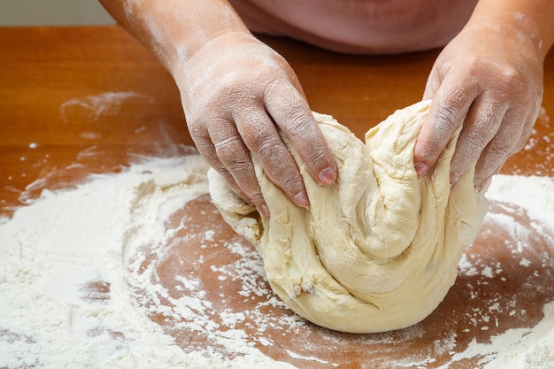 Foto de handen van een joodse vrouw kneden het deeg voor rieten challahs voor de feestdag op tafel