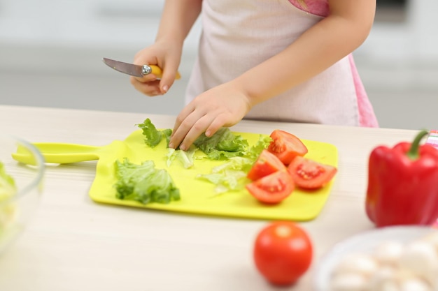 De handen van een klein meisje snijden groenten op een bord