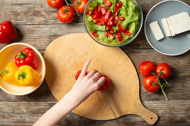 De handen van een meisje snijden tomates op een houten lijst