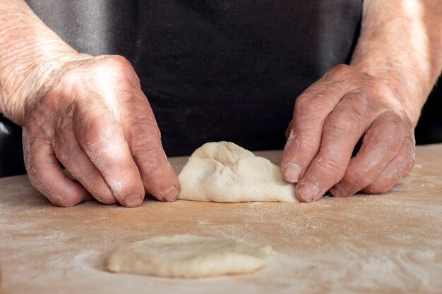 De handen van een oude vrouw maken deeg van deeg